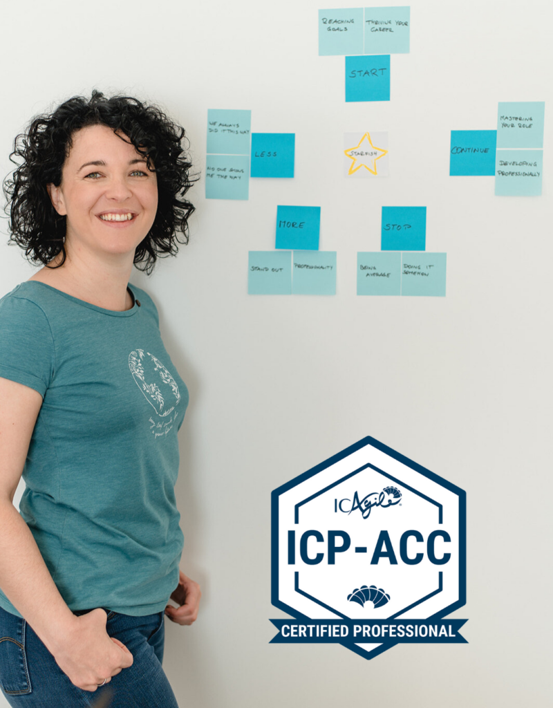 Paulina Hornbachner steht vor einer Wand mit Post Its. Der Badge für das Zertifikat "Certified Professional Agile Coaching" ist zu sehen